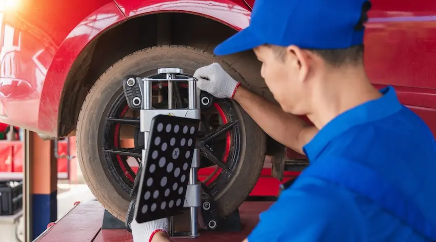 A mechanic in a blue uniform and cap attaches a wheel alignment tool to the rim of a red vehicle representing the type of auto repair work that can result in repair-related diminished value even after a car is restored to working condition in Georgia.
