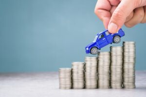A hand places a small blue toy truck on top of ascending stacks of coins symbolizing the financial recovery process of recouping repair-related diminished value after a vehicle has been damaged and repaired with help from Claims Concierge.